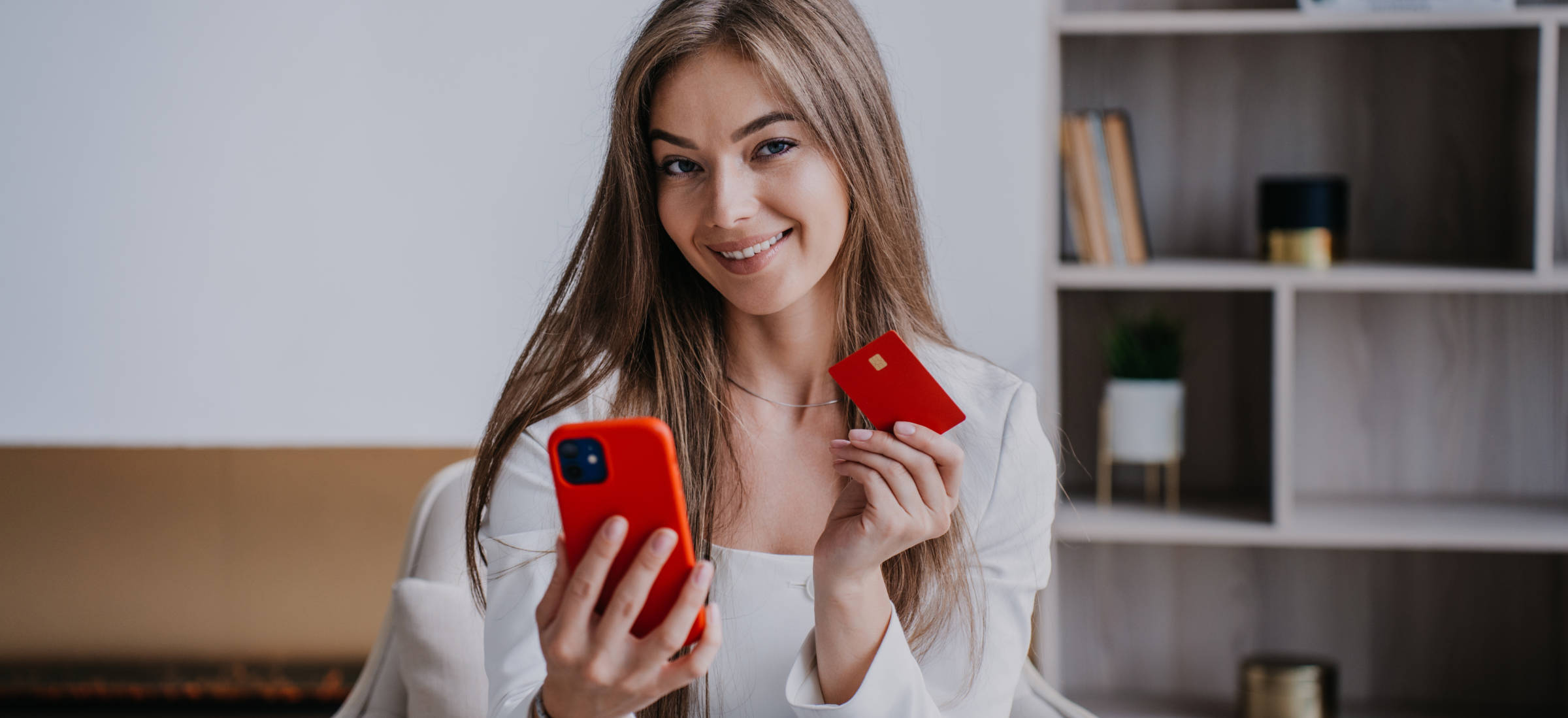 Contented beautiful blonde young woman in business suit, sitting in a comfortable chair in the office, talking by phone, showing off new bank card with salary. Excited entrepreneur gets money distant.