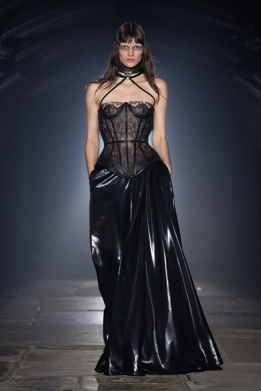 Modelka w eleganckiej, czarnej sukni z koronkowym gorsetem i błyszczącą, luźną spódnicą.