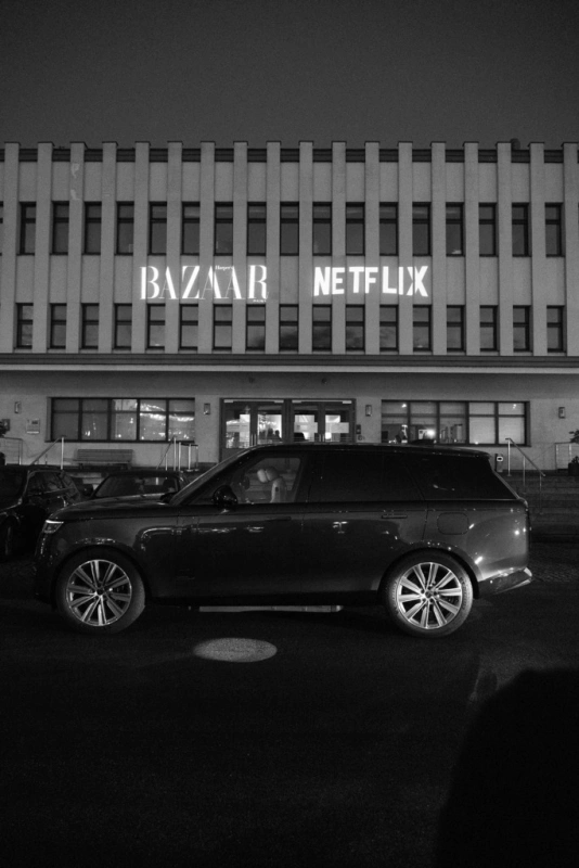 Na zdjęciu widoczny jest czarny samochód zaparkowany przed Muzeum Emigracji w Gdyni z neonami "BAZAR" i "NETFLIX".