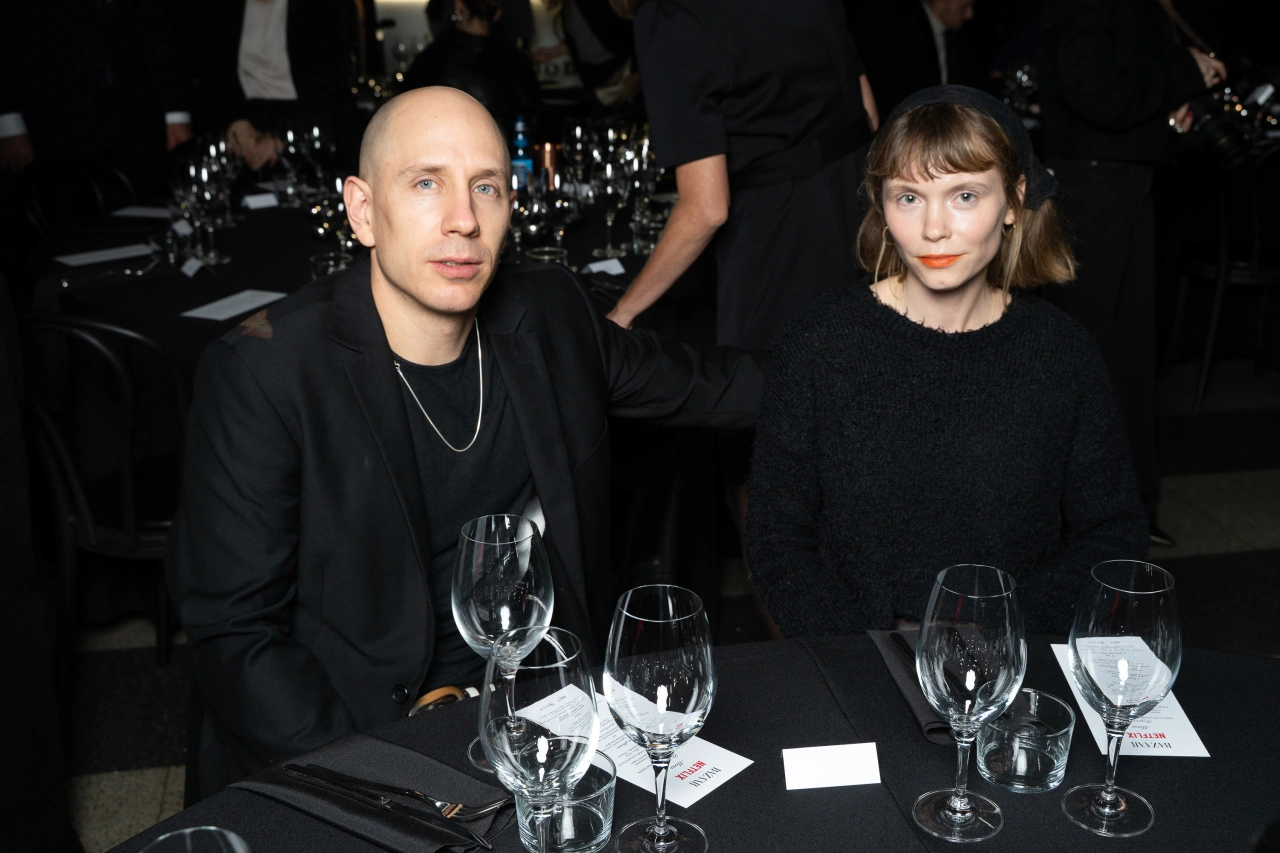Maciej Edelman i Agata Trzebuchowska siedzą przy stole, otoczeni kieliszkami i innymi gośćmi.