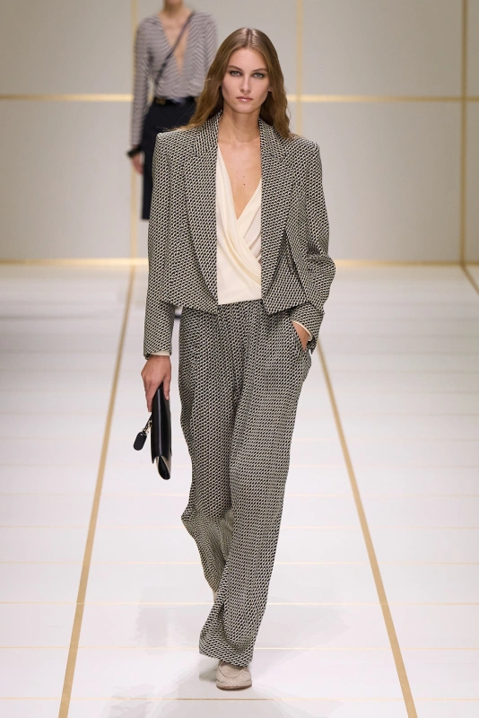Modelka w eleganckim zestawie w czarno-białym wzorze, w formie luźnego garnituru, z torebką w ręce.