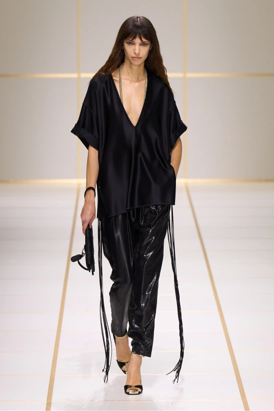 Modelka na wybiegu w eleganckiej czarnej koszuli i błyszczących spodniach. Styl minimalistyczny, nowoczesny look.