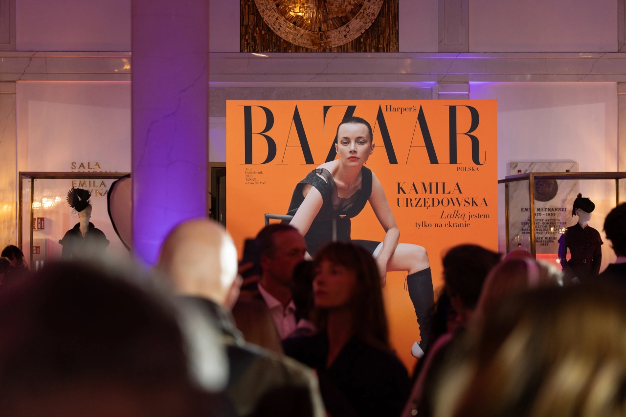 Na tle tłumu widać dużą okładkę magazynu „Harper's Bazaar Polska” z wizerunkiem modelki.