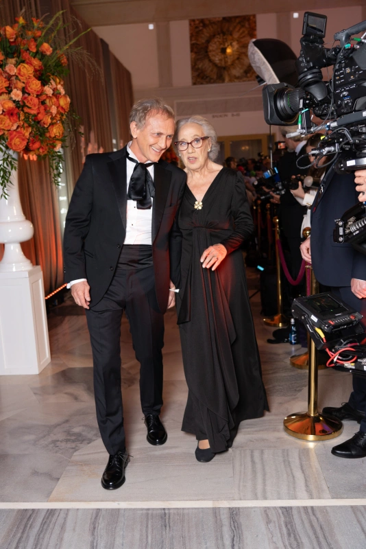 Andrzej Chyra i Maja Komorowska spacerują razem po czerwonym dywanie, ubrani w eleganckie stroje.