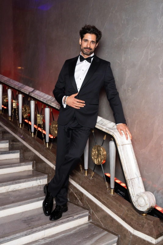 Maciej Kawalski w eleganckim garniturze, oparty na balustradzie w stylowej scenerii.