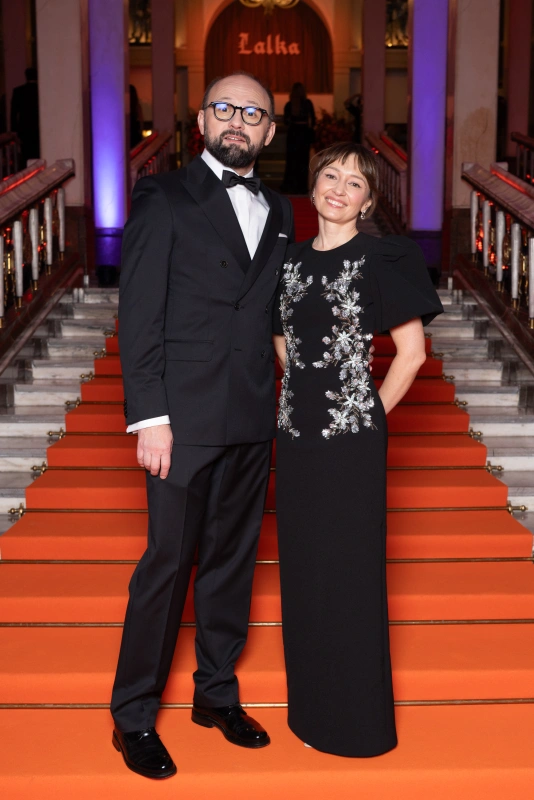 Radosław Drabik i Dominika Buck w eleganckich strojach na pomarańczowym dywanie przed wejściem do budynku.