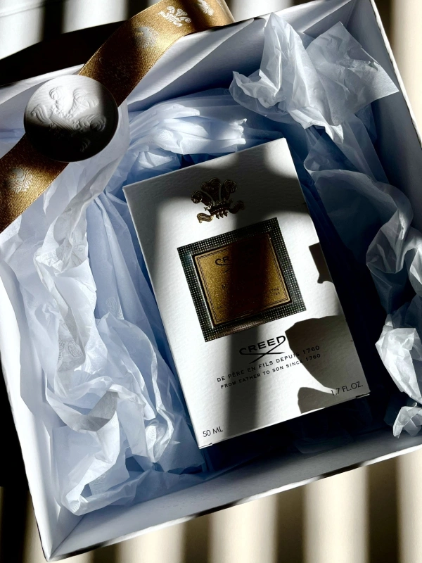 Perfumy Creed umieszczone w eleganckim opakowaniu z białym papierem i złotą wstążką.