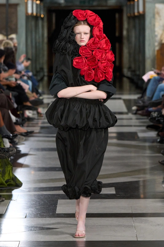 Modelka prezentuje kreację Simone Rocha wiosna-lato 2027, z czarną suknią i kolorowymi detalami z róż.